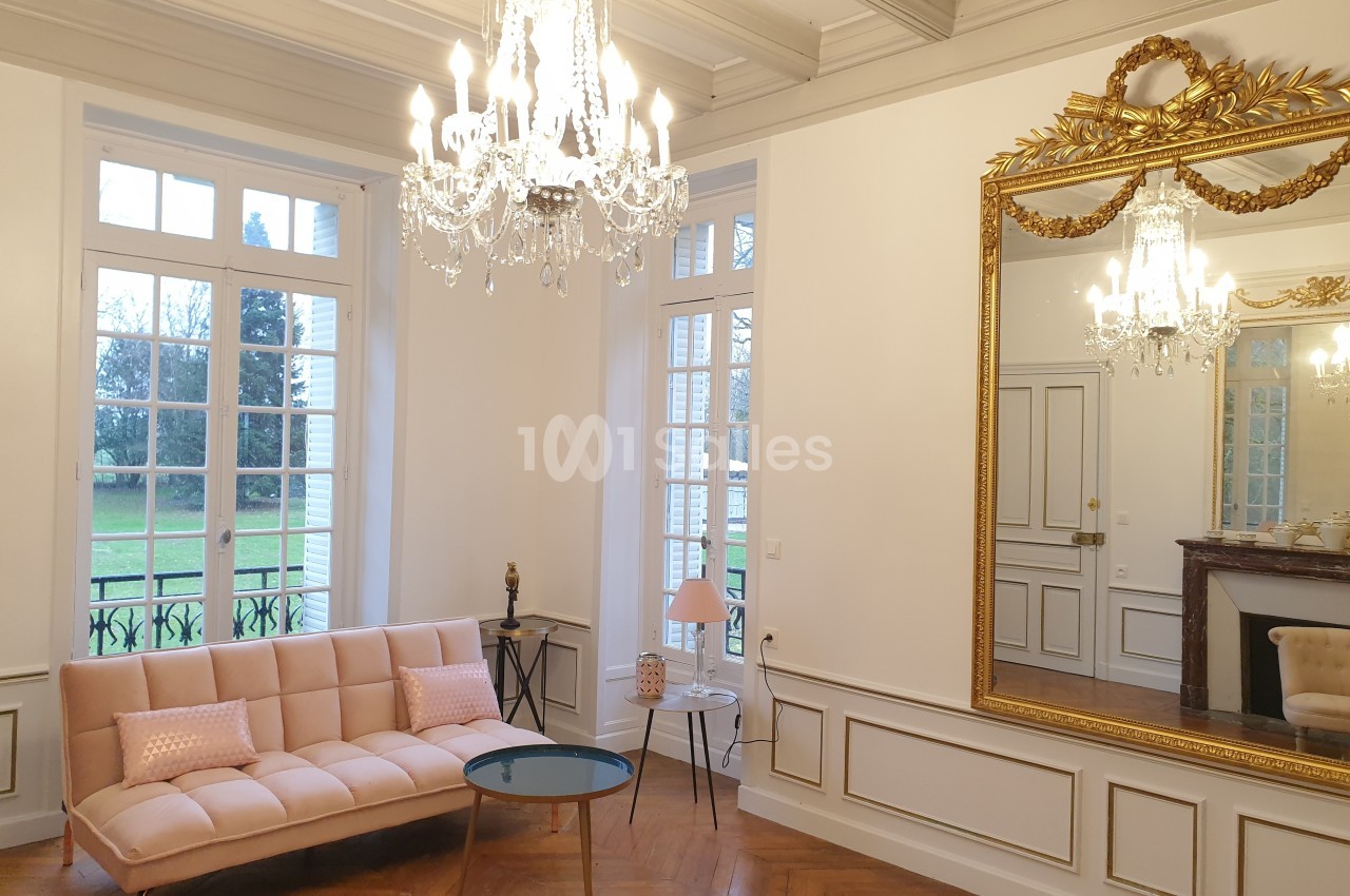Salon lumineux avec parquet en bois, canapé rose, table basse, miroir doré et lustres en cristal.