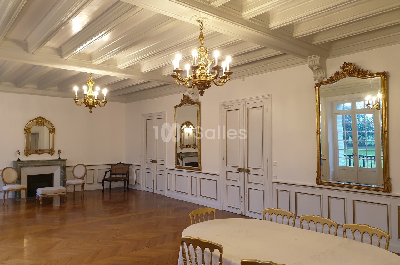 Salle élégante avec parquet en bois, moulures au plafond, lustres dorés, miroirs et table entourée de chaises.