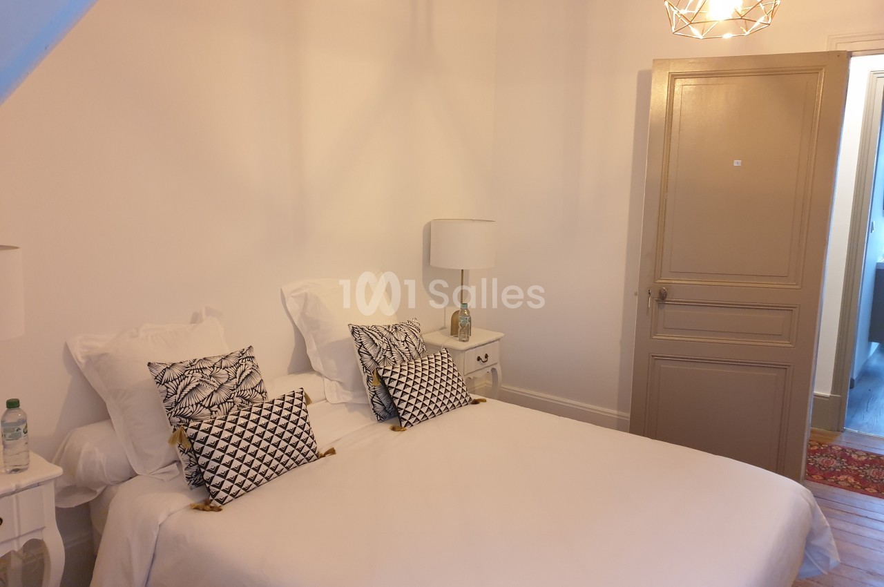 Chambre lumineuse avec un lit double, des coussins décoratifs, deux lampes de chevet et une porte beige.