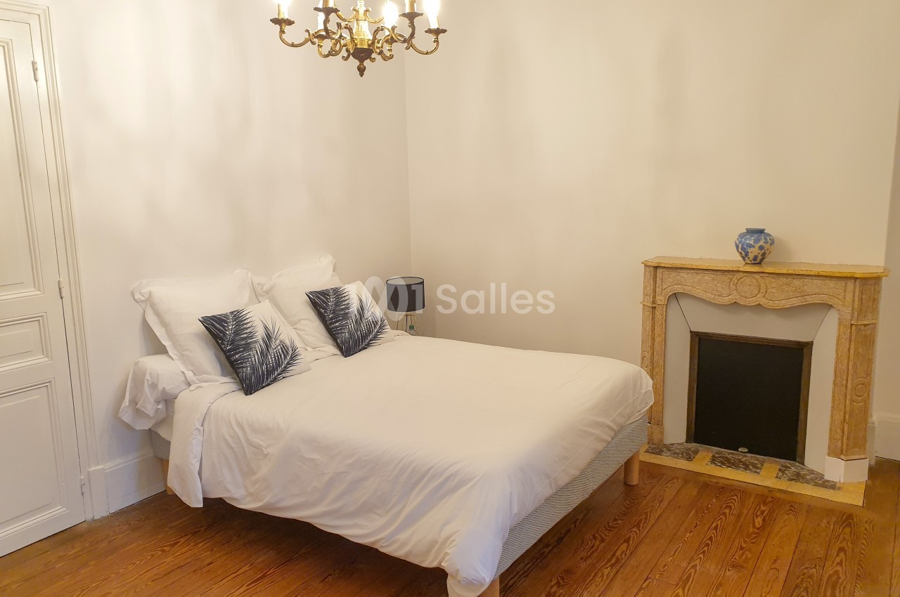 Chambre avec un lit double, cheminée décorative, parquet en bois et lustre suspendu.