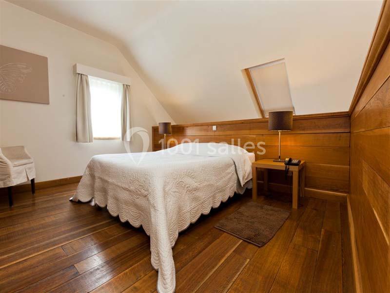Chambre avec lit double, parquet en bois, murs partiellement lambrissés, fenêtre et lucarne apportant de la lumière…