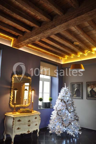 Plafond en bois apparent dans une pièce décorée avec un sapin de Noël blanc, un miroir et des meubles anciens.