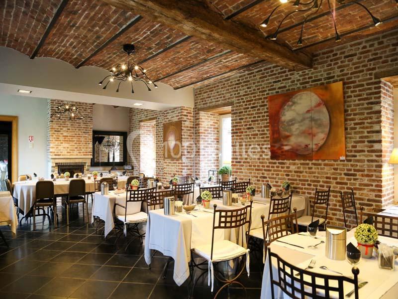 Salle de restaurant avec murs en briques, plafond en poutres apparentes et tables dressées avec nappes blanches.