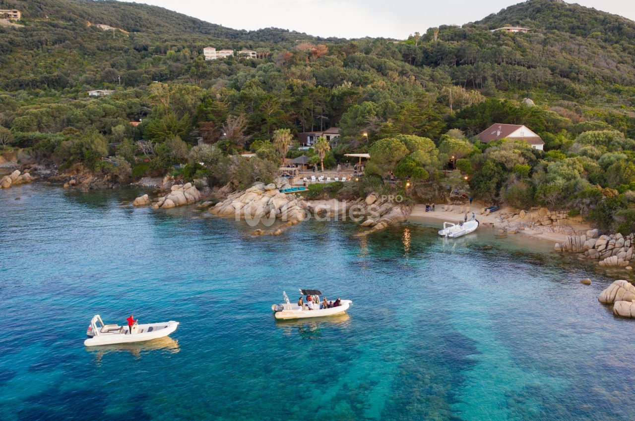 Deux bateaux amarrés près d'une côte rocheuse bordée de végétation dense et de maisons sur les collines.