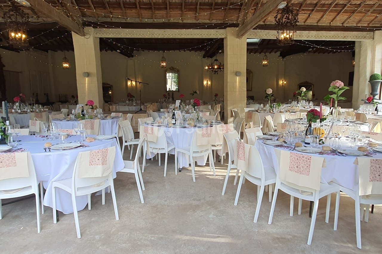 Salle de réception décorée avec des tables rondes dressées, nappes blanches et fleurs colorées.
