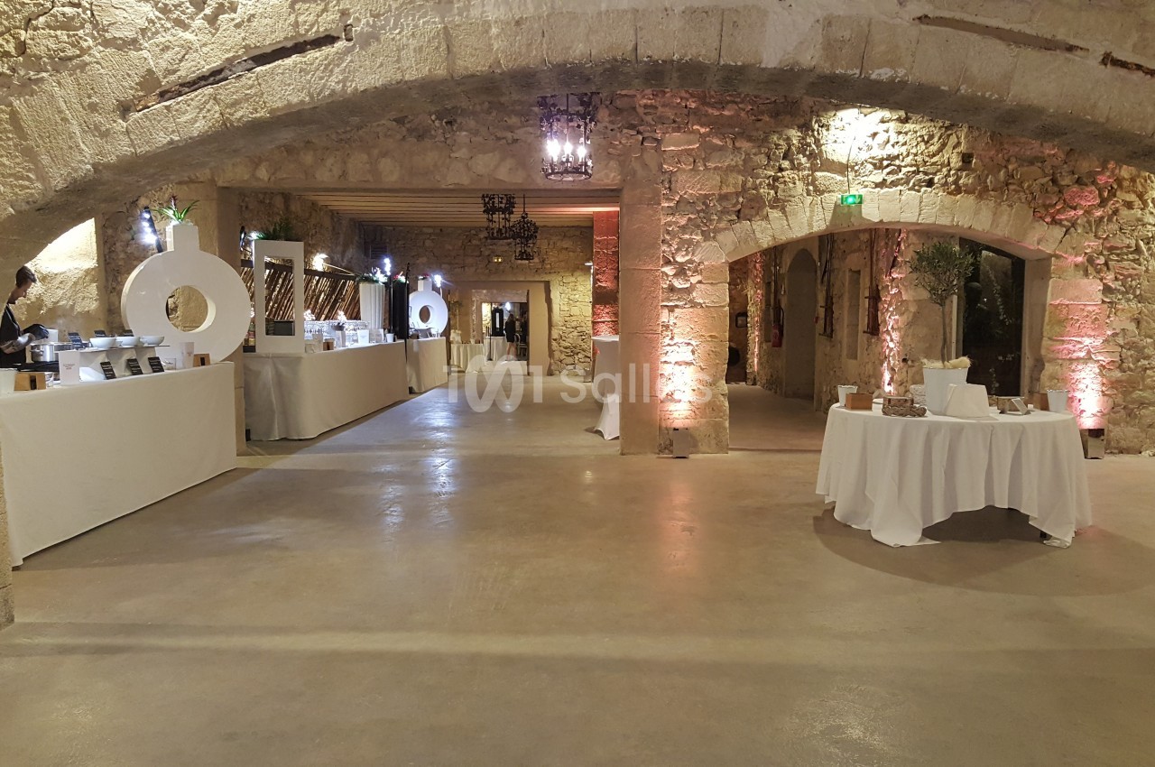 Salle en pierre avec arches, tables décorées et stands alignés, éclairage chaleureux créant une ambiance conviviale.