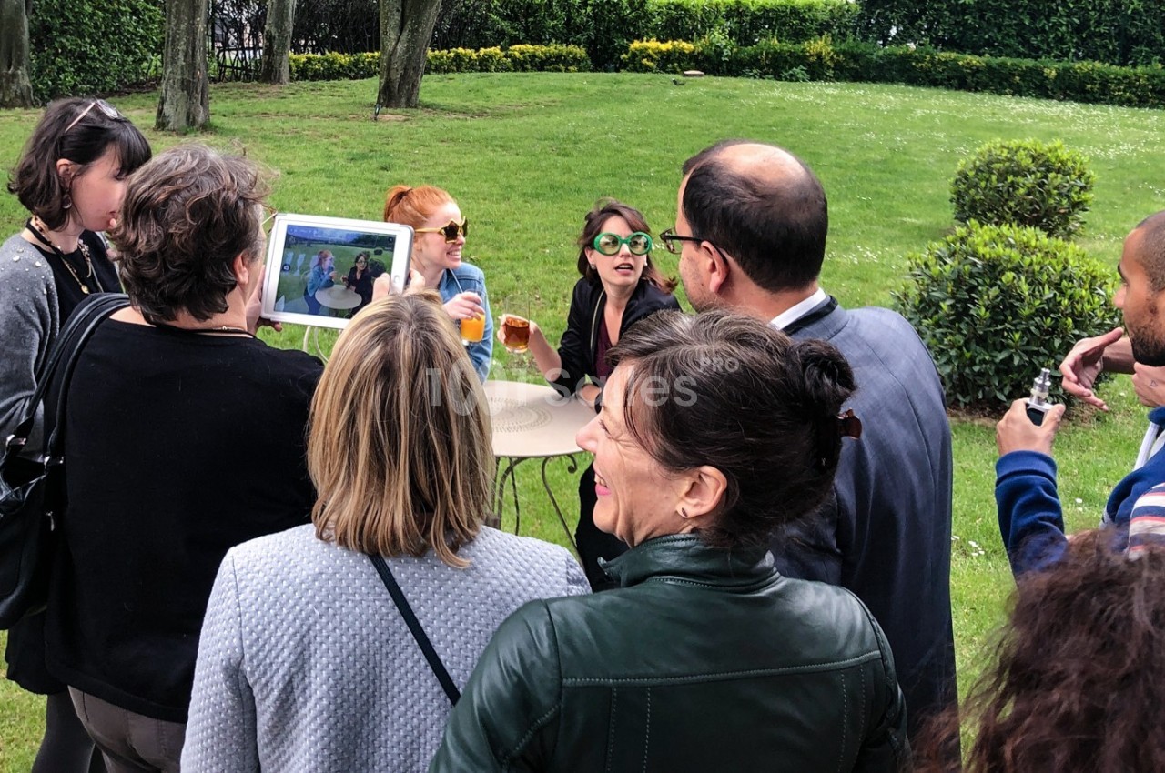 Un groupe de personnes discute autour d'une table en extérieur, certaines regardant une tablette.