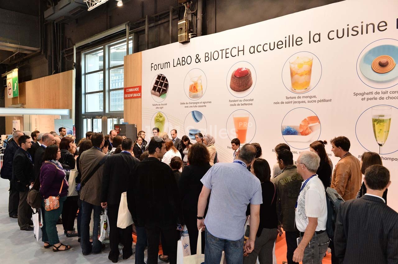 Un groupe de personnes observe une démonstration culinaire devant un stand lors d'un événement professionnel.