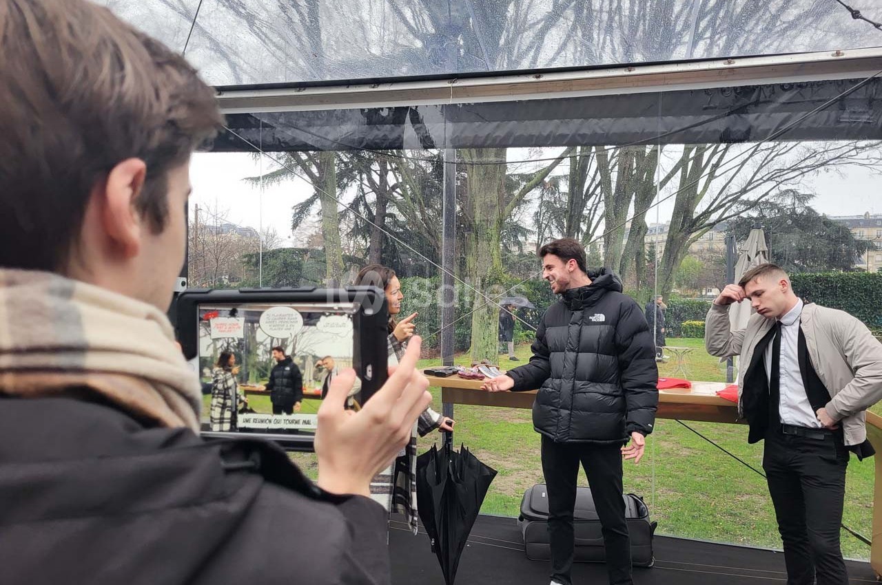 Un homme est filmé avec une tablette tandis qu'il discute avec deux autres personnes sous une structure transparente.