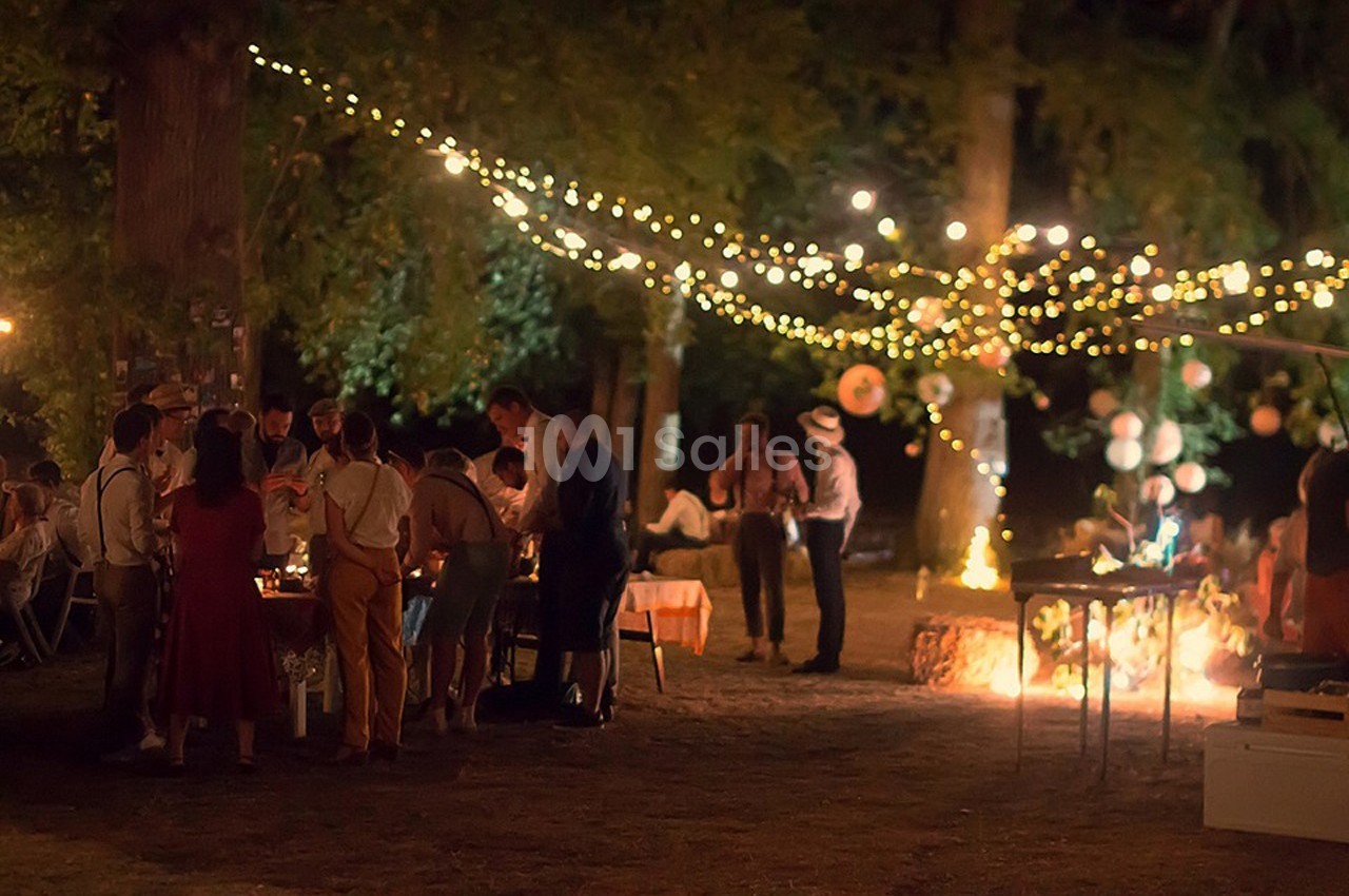 Groupe de personnes réunies en soirée dans un jardin éclairé par des guirlandes lumineuses suspendues aux arbres.