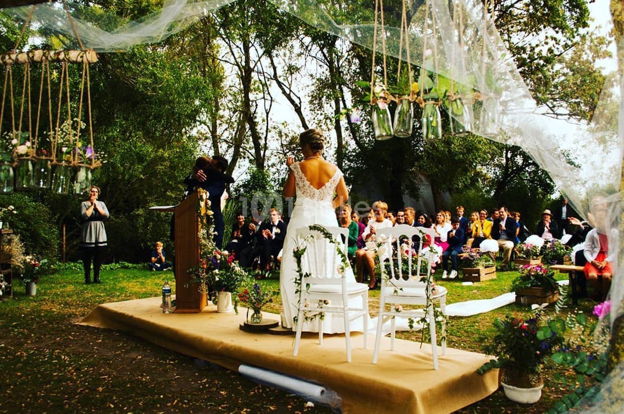 Cérémonie de mariage en plein air avec une mariée debout face à l'officiant, entourée d'invités assis.