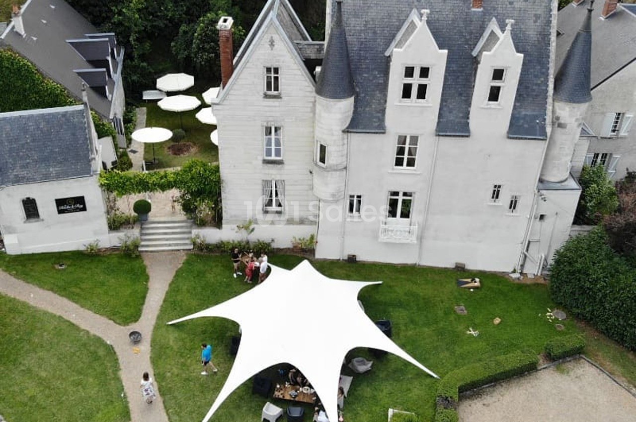 Vue aérienne d'un manoir blanc avec une grande tente blanche dans le jardin, entouré de verdure et de chemins.