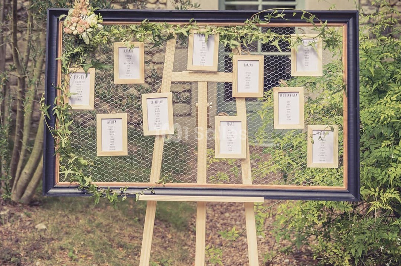 Tableau de plan de table de mariage avec cadres suspendus sur un grillage décoré de feuillage et de fleurs.
