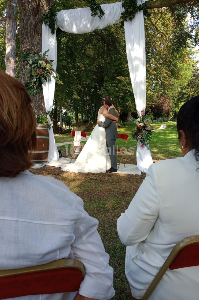 Un couple s'embrasse sous une arche décorée de fleurs lors d'une cérémonie de mariage en plein air.