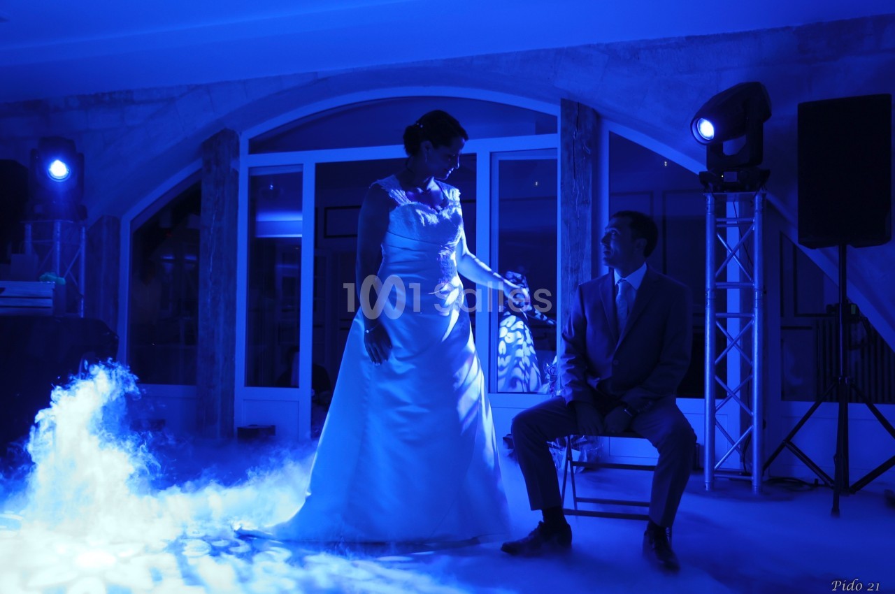 Une mariée en robe blanche et un homme en costume assis, éclairés par une lumière bleue dans une ambiance festive.