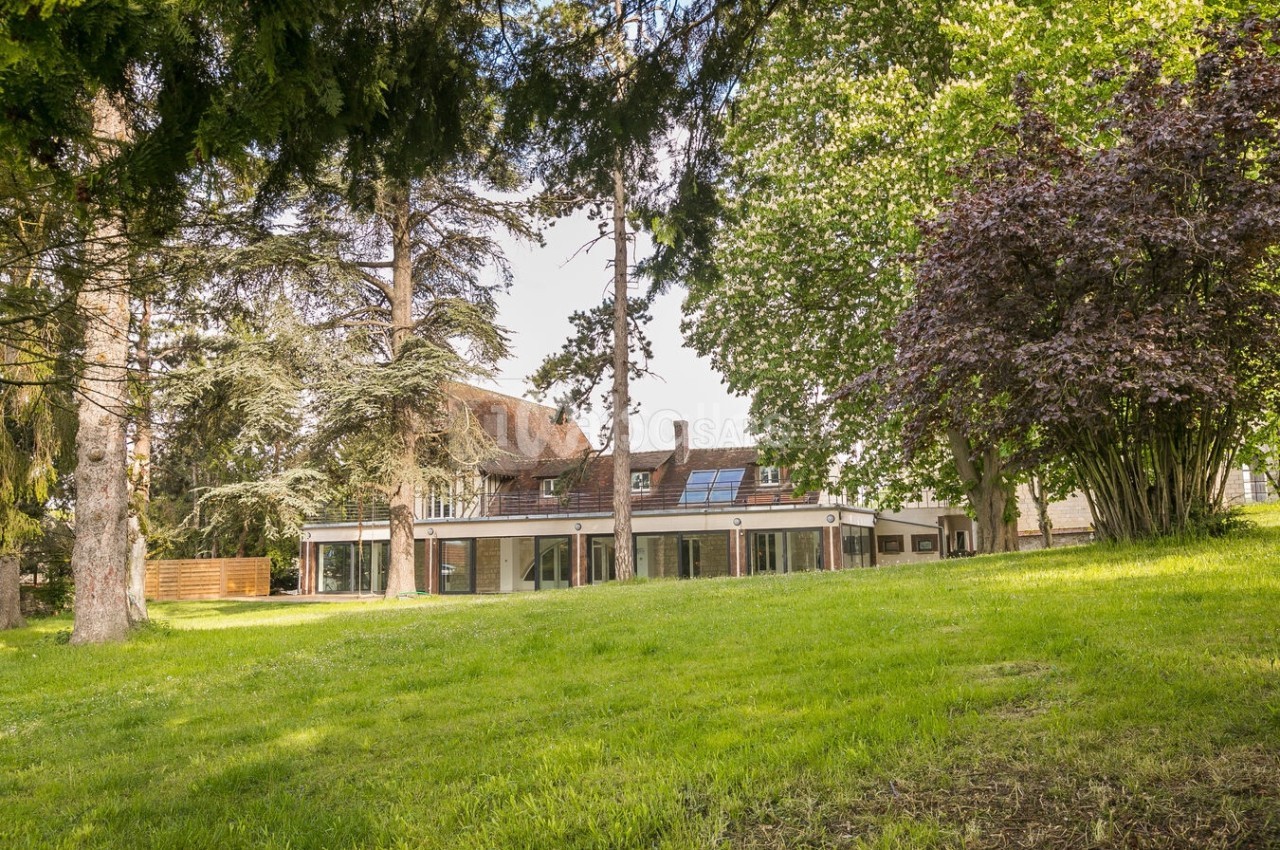 Grande maison entourée d'arbres et d'une pelouse verdoyante, vue depuis un jardin spacieux.