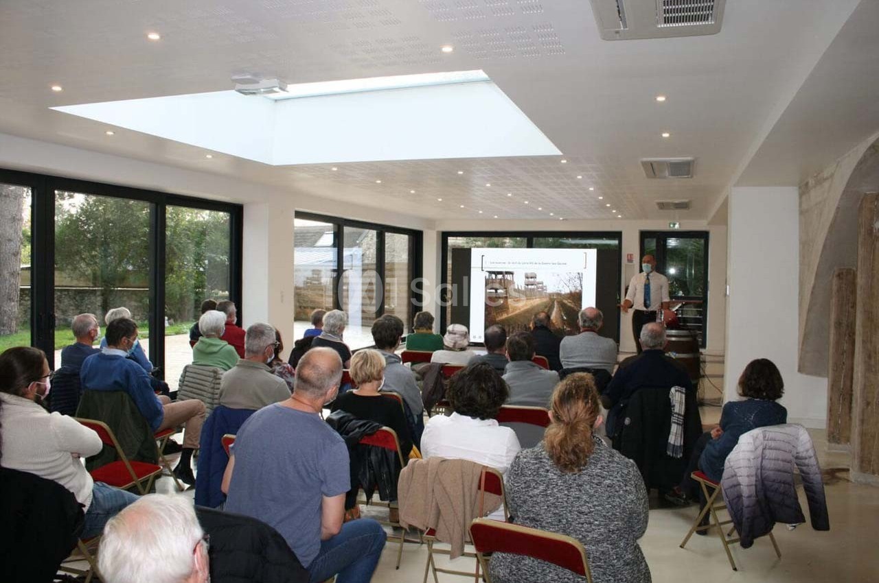 Un groupe de personnes assises assiste à une présentation avec un écran projetant une image dans une salle lumineuse.