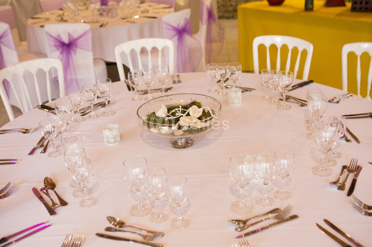 Table ronde dressée pour un événement, avec nappes blanches, verres, couverts et centre de table décoratif.