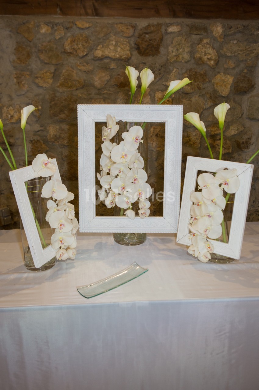 Arrangement floral avec des orchidées blanches et des callas dans des vases, encadrés par des cadres blancs, sur une table.