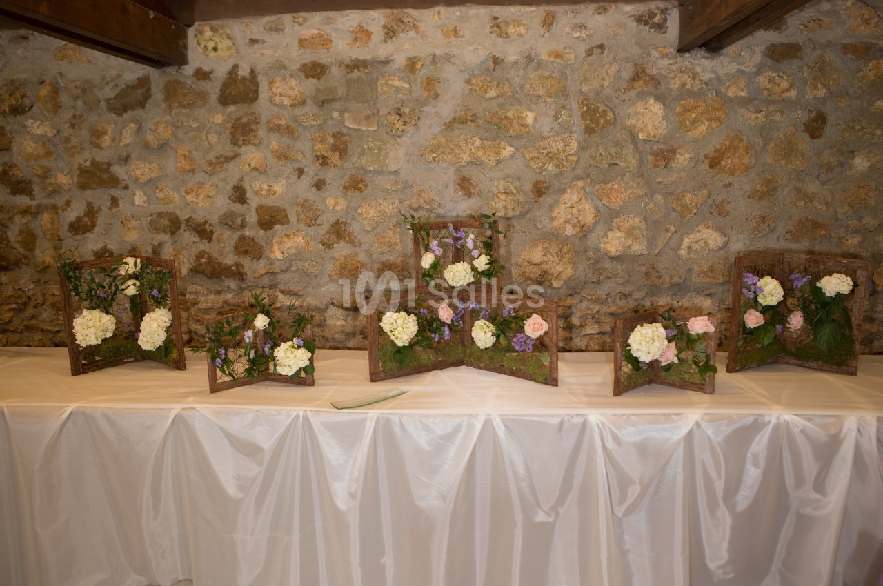 Arrangements floraux sur des supports en bois disposés sur une table recouverte d'une nappe blanche devant un mur en pierre.