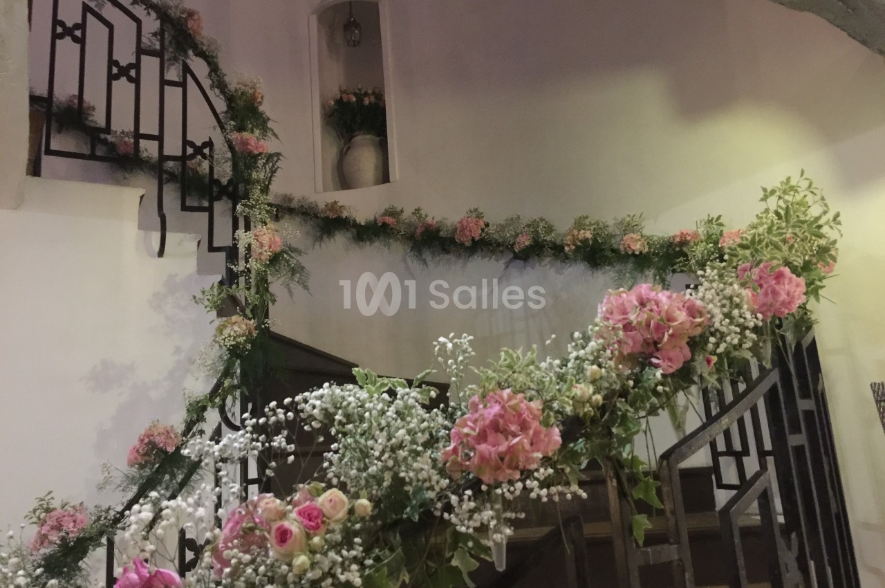 Escalier en colimaçon décoré de fleurs roses et blanches avec des feuillages, dans un intérieur lumineux.