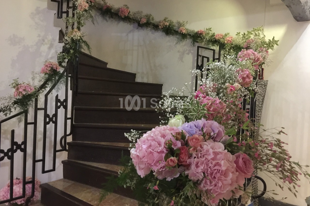 Escalier décoré de guirlandes de fleurs roses et blanches, avec des bouquets disposés au premier plan.