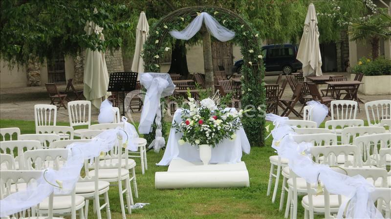 Chaises blanches décorées et arche fleurie installées en extérieur pour une cérémonie de mariage.