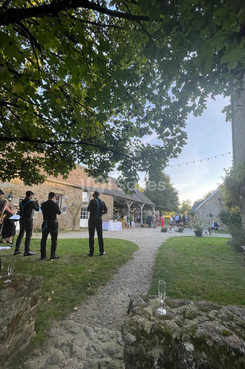 Personnes rassemblées dans une cour en pierre avec tables dressées, arbres et guirlandes lumineuses en arrière-plan.