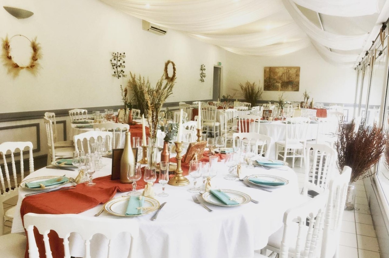 Salle de réception décorée avec des tables rondes, nappes blanches, chemins de table rouges et éléments floraux.