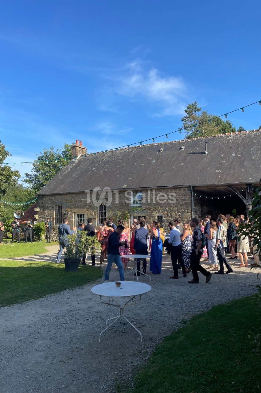 Groupe de personnes rassemblées devant une maison en pierre dans un jardin par une journée ensoleillée.