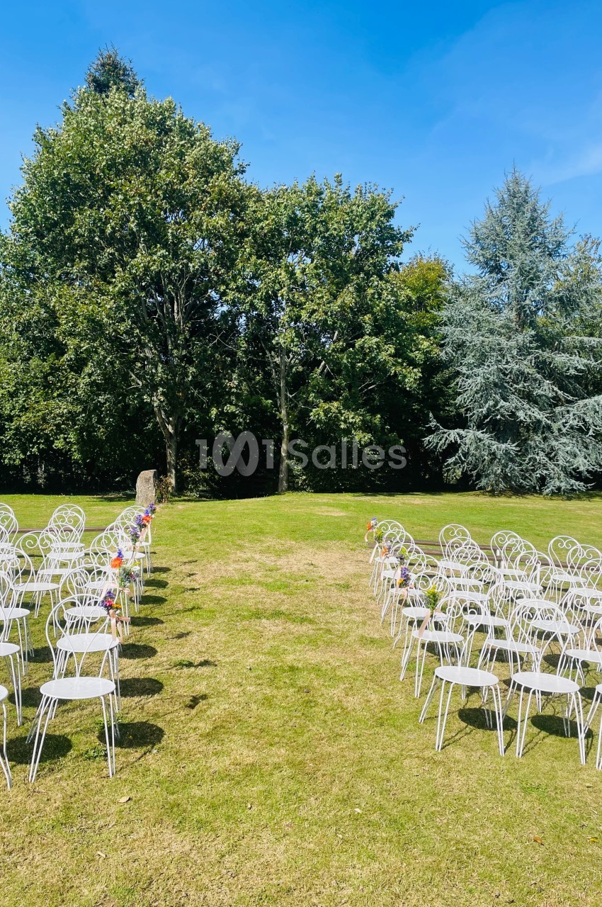 Chaises blanches alignées en extérieur, formant une allée centrale sur une pelouse, entourée d'arbres.