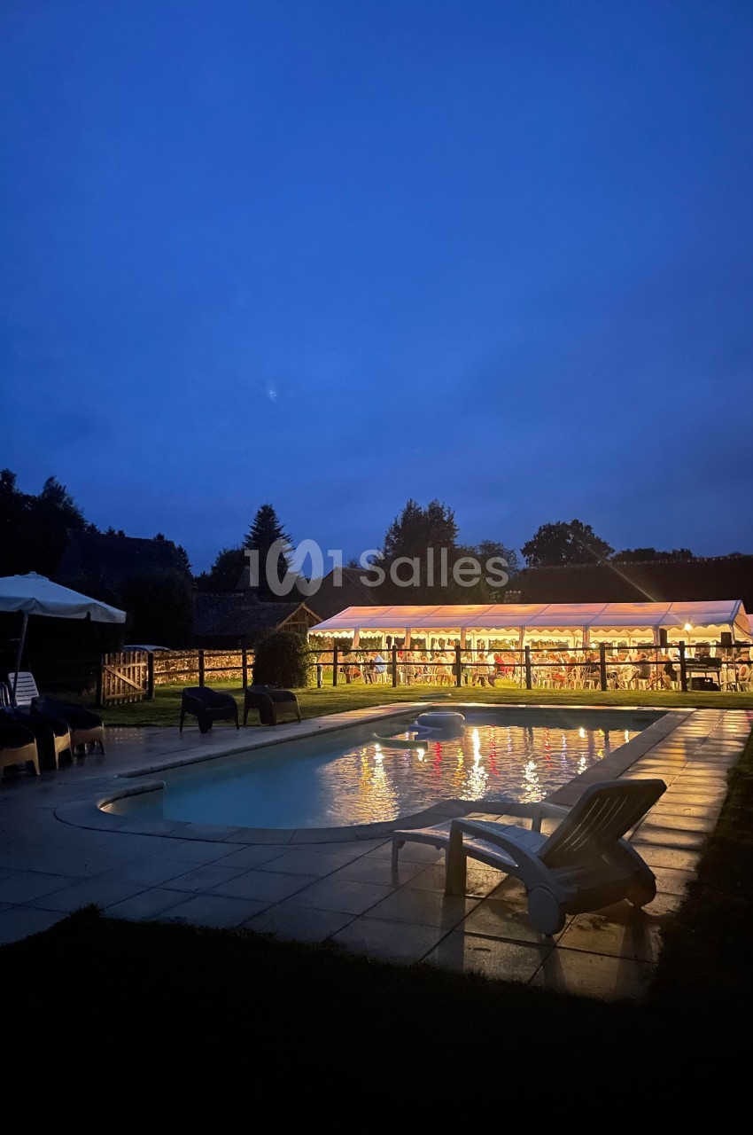 Piscine éclairée au crépuscule avec des chaises longues et un bâtiment illuminé en arrière-plan.