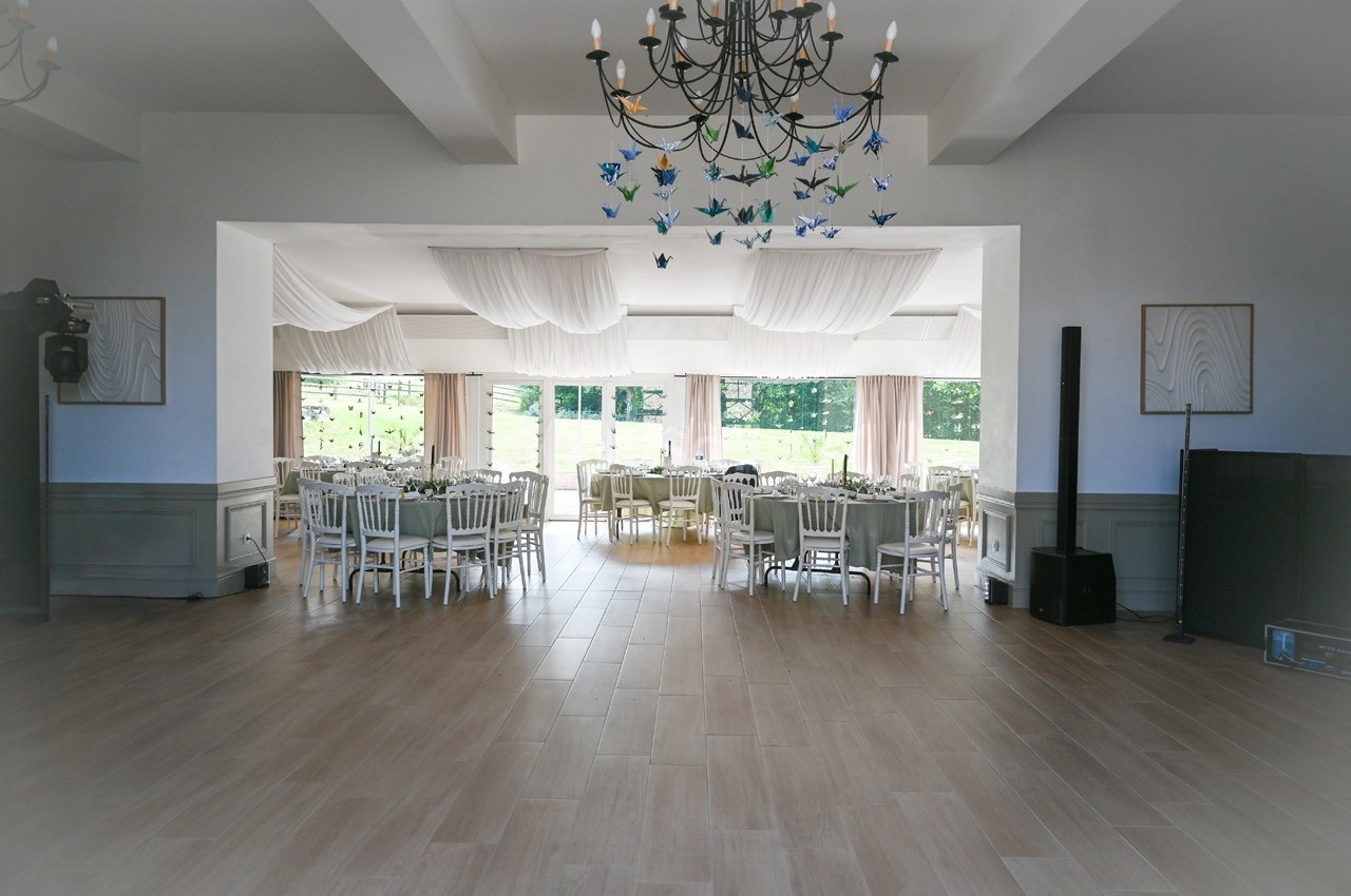 Salle de réception lumineuse avec tables dressées, chaises blanches, lustre et décorations suspendues en papier.