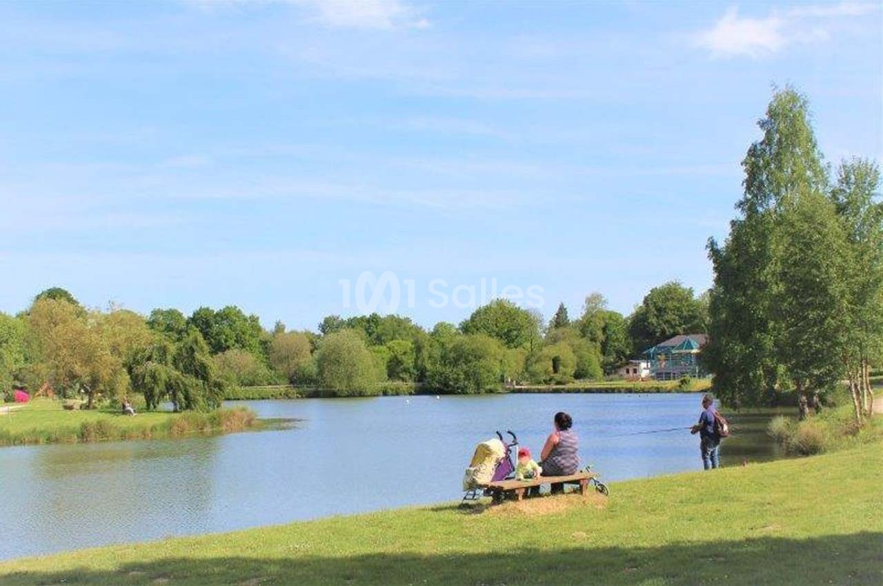 Deux personnes assises sur un banc près d'un lac entouré d'arbres, sous un ciel dégagé.