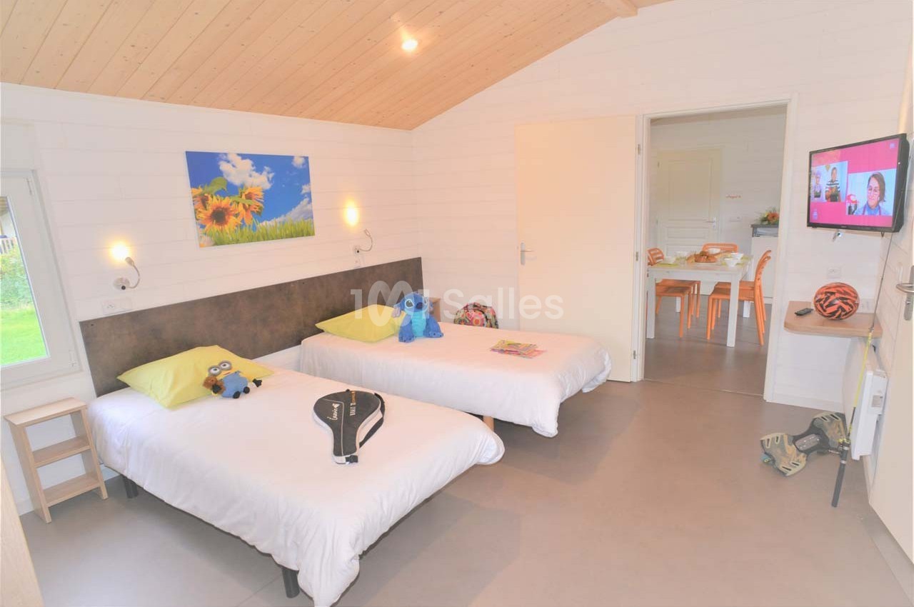 Chambre lumineuse avec deux lits simples, jouets posés dessus, et vue sur une table dans une pièce adjacente.