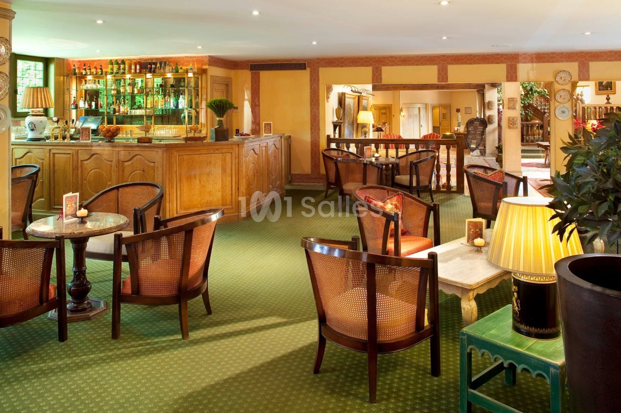 Salle de bar lumineuse avec comptoir en bois, tables rondes, chaises en rotin et décoration chaleureuse.