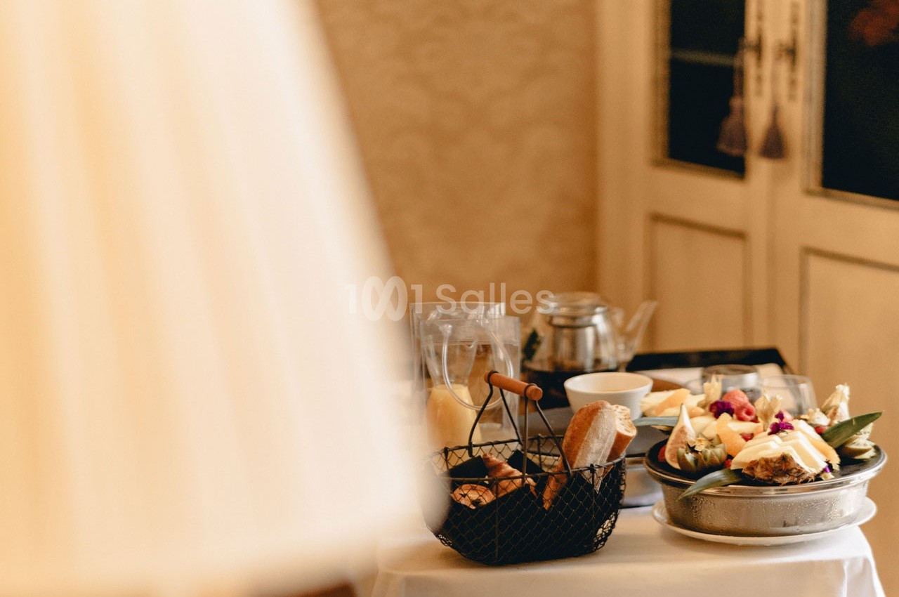 Petit-déjeuner servi sur une table avec viennoiseries, fruits, théière et assiettes, dans un décor chaleureux.