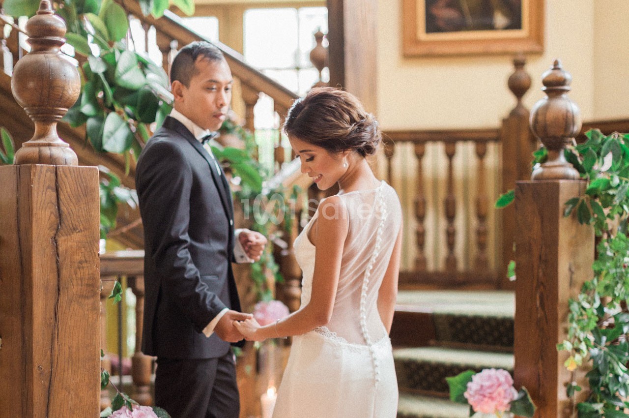 Un couple en tenue de mariage se tient la main devant un escalier décoré de plantes et de fleurs.