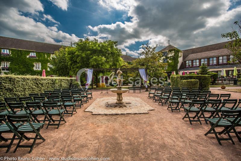 Chaises disposées en rangées face à une fontaine dans une cour extérieure entourée de bâtiments et de végétation.