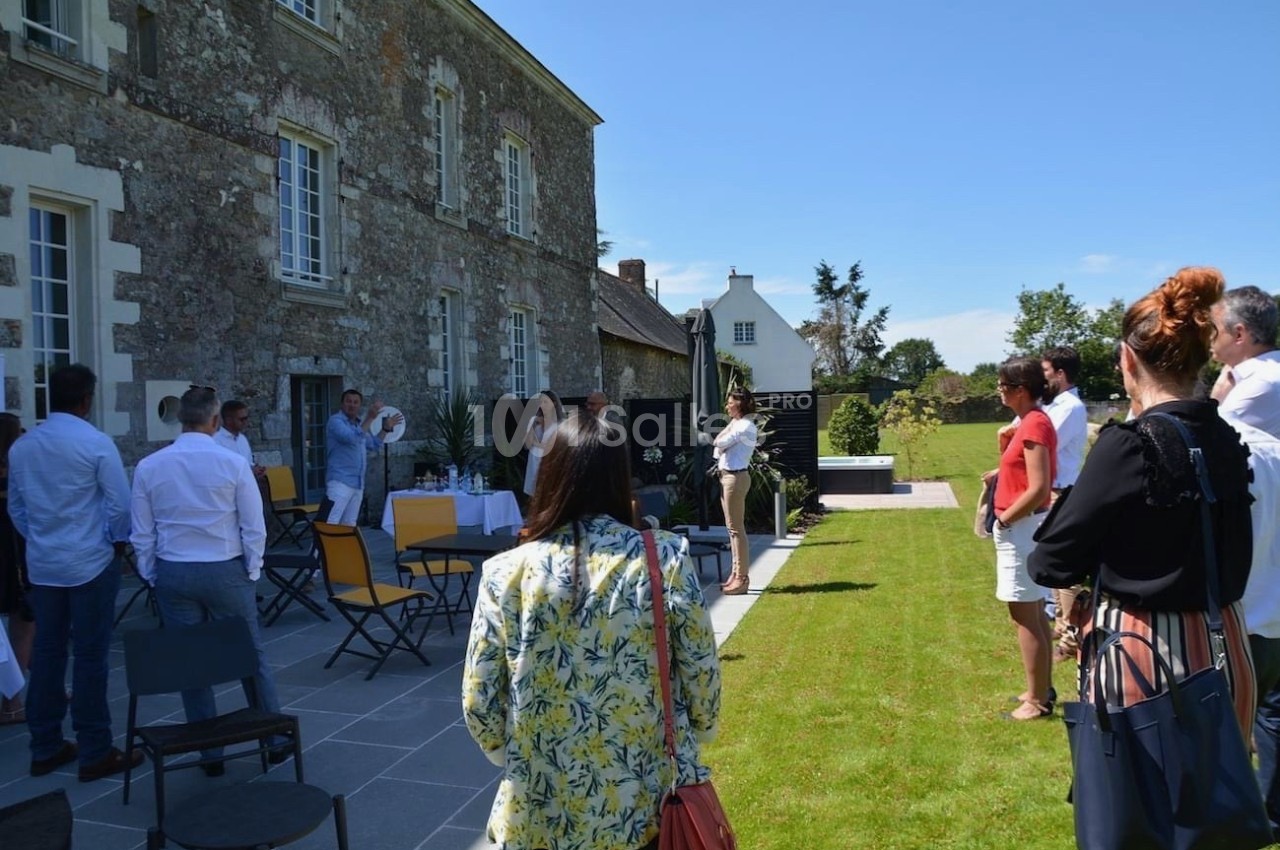 Un groupe de personnes debout et assises dans un jardin, près d'un bâtiment en pierre, par une journée ensoleillée.