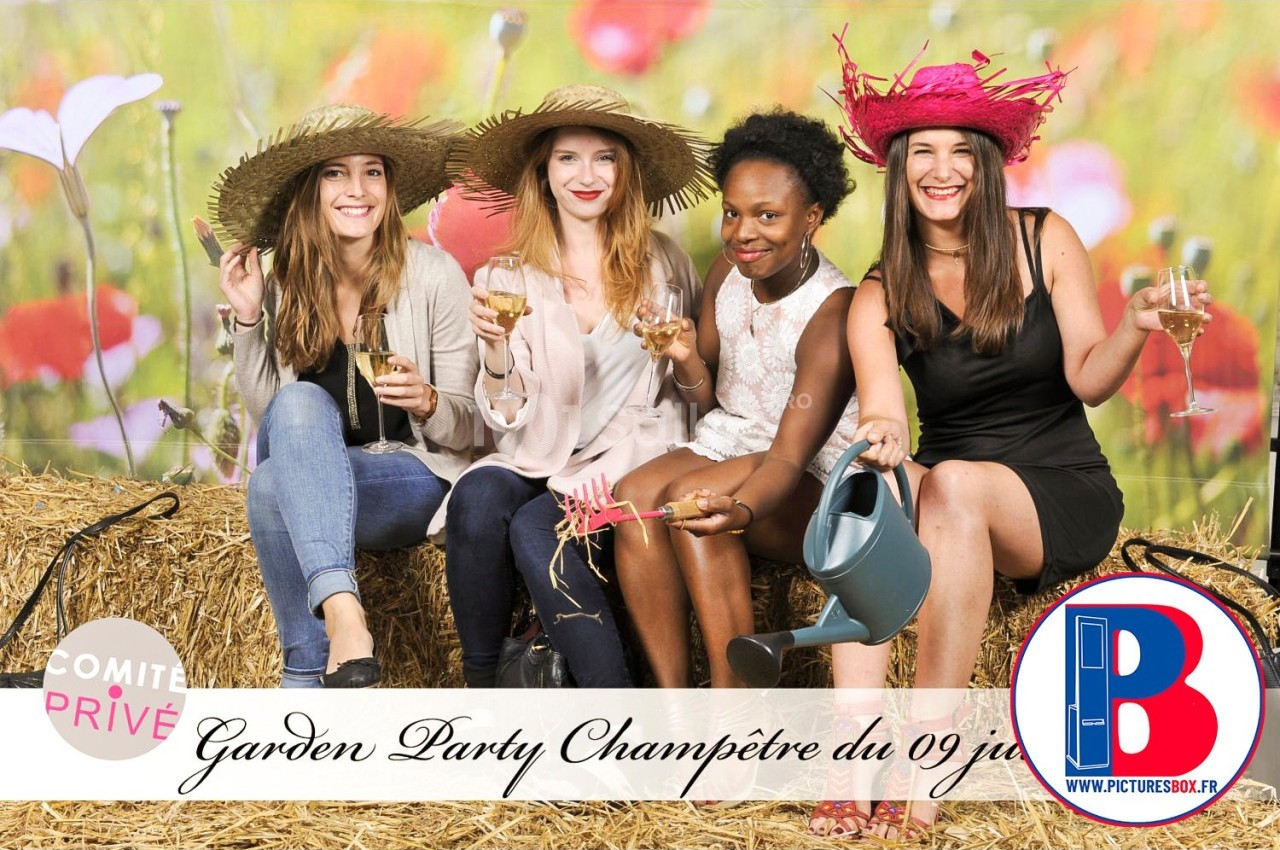 Quatre femmes souriantes assises sur des bottes de paille, portant des chapeaux et tenant des objets festifs.