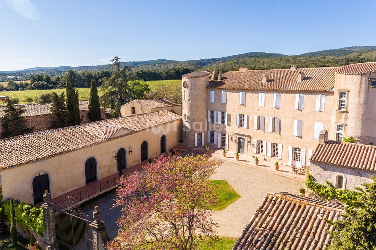 Vue aérienne d'un domaine avec un bâtiment historique, une cour centrale et des collines verdoyantes en arrière-plan.