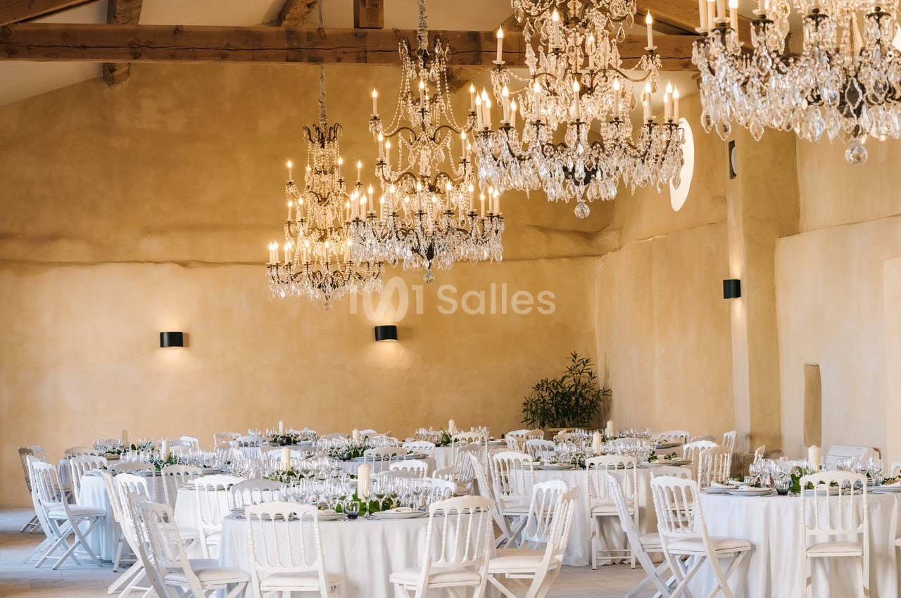 Salle de réception lumineuse avec des tables rondes dressées et des lustres en cristal suspendus au plafond.