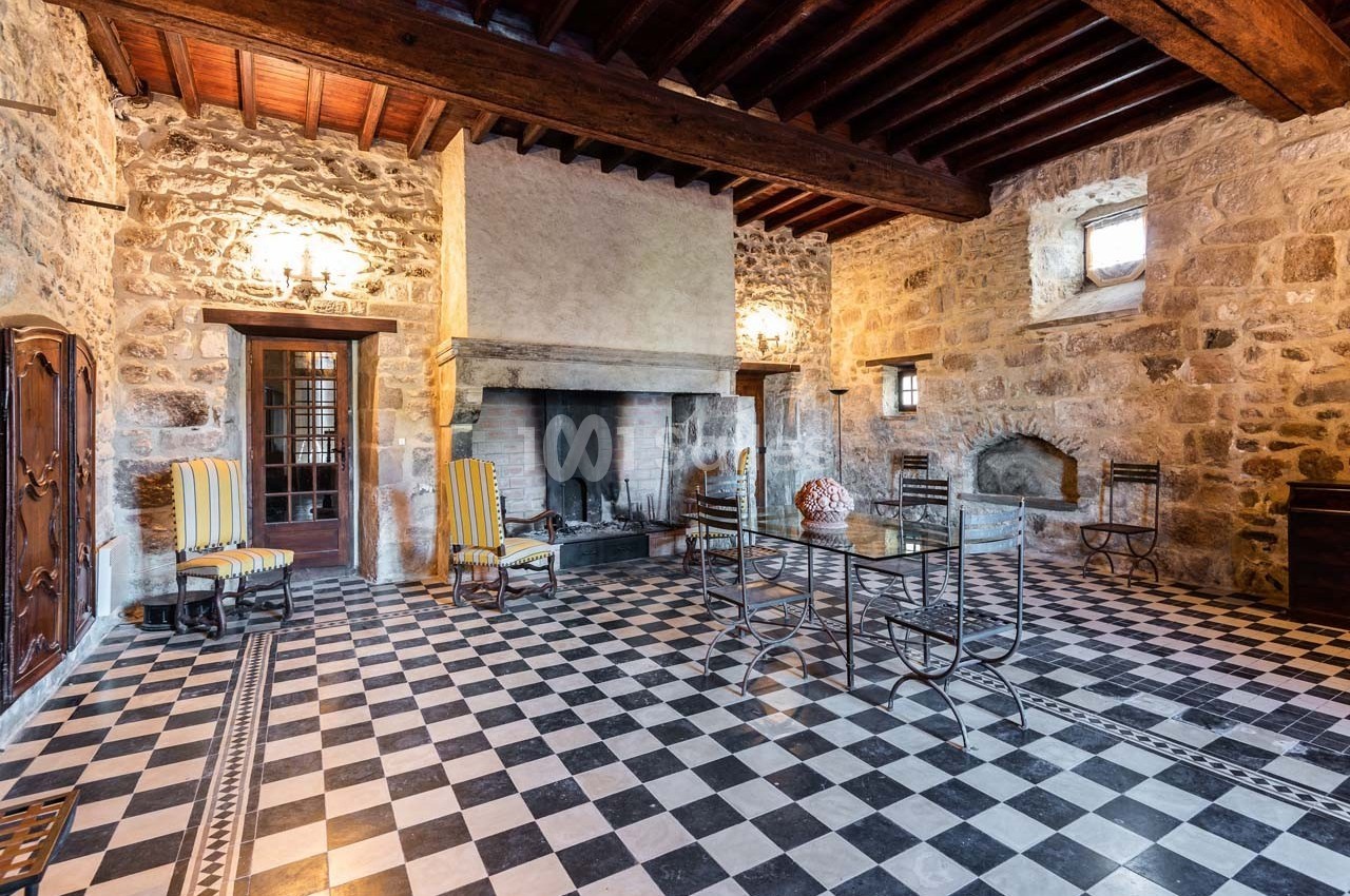Salle rustique avec murs en pierre, cheminée, plafond en bois, sol à damier noir et blanc, et mobilier en métal.