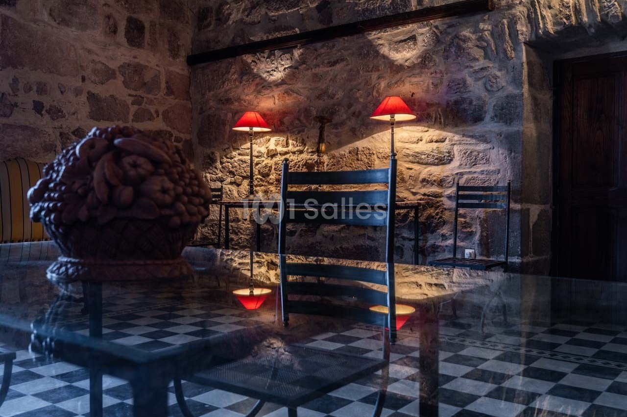 Salle en pierre avec éclairage tamisé, table en verre réfléchissant un panier décoratif et des chaises en métal.