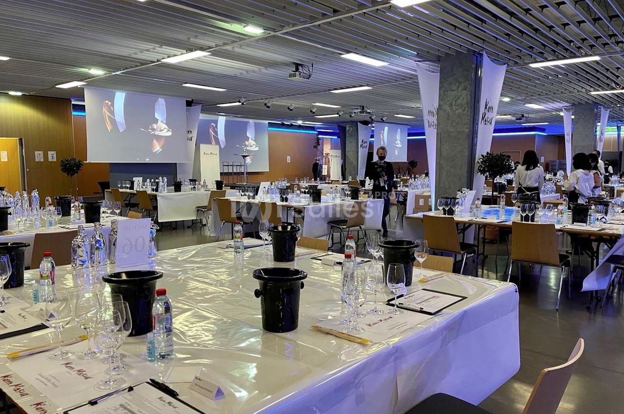 Salle de dégustation aménagée avec des tables dressées, verres, crachoirs et documents, prête pour un événement.