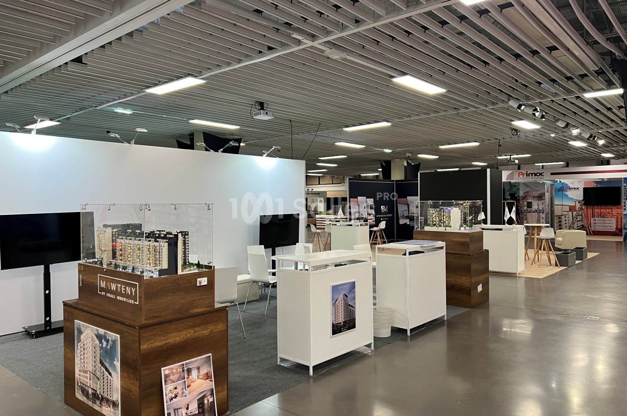 Stands d'exposition dans un espace intérieur avec maquettes architecturales et panneaux d'information.