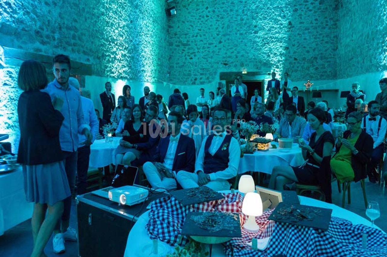 Des invités assis et debout dans une salle en pierre éclairée de lumières bleues, lors d'un événement festif.