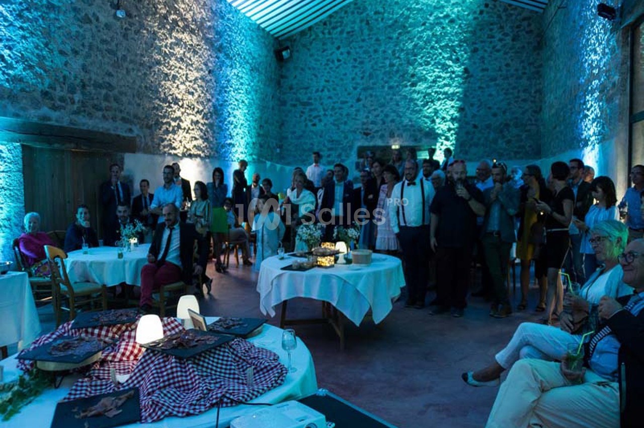 Groupe de personnes rassemblées dans une salle en pierre éclairée par des lumières bleues, avec des tables décorées.