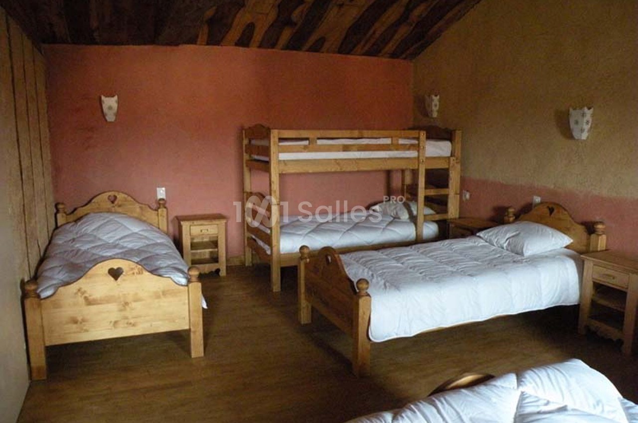 Chambre avec lits en bois, dont un superposé, sur un sol en parquet et murs aux tons chauds.